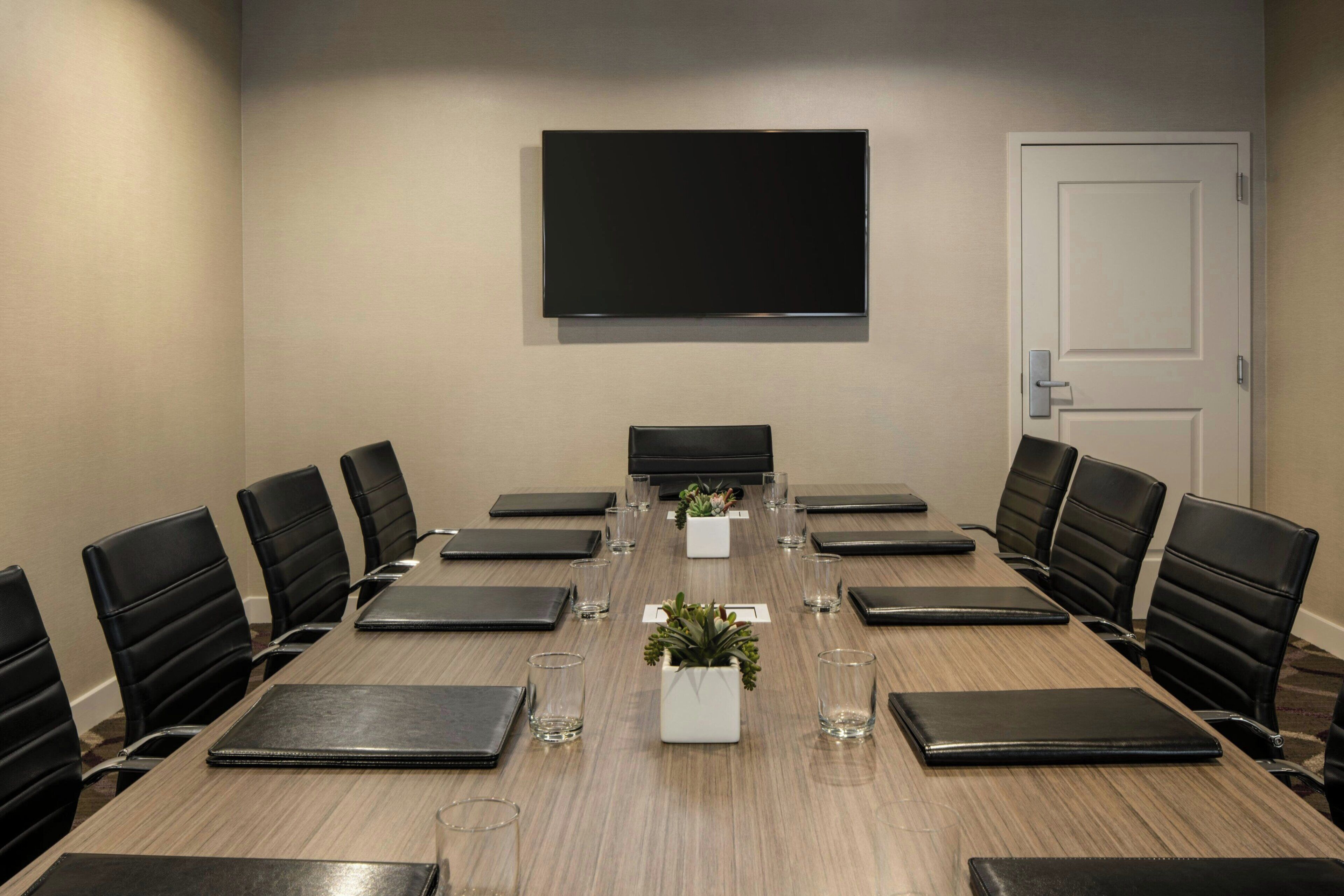 Una sala de conferencias con una larga mesa, sillas negras, un televisor de pantalla plana y una puerta.