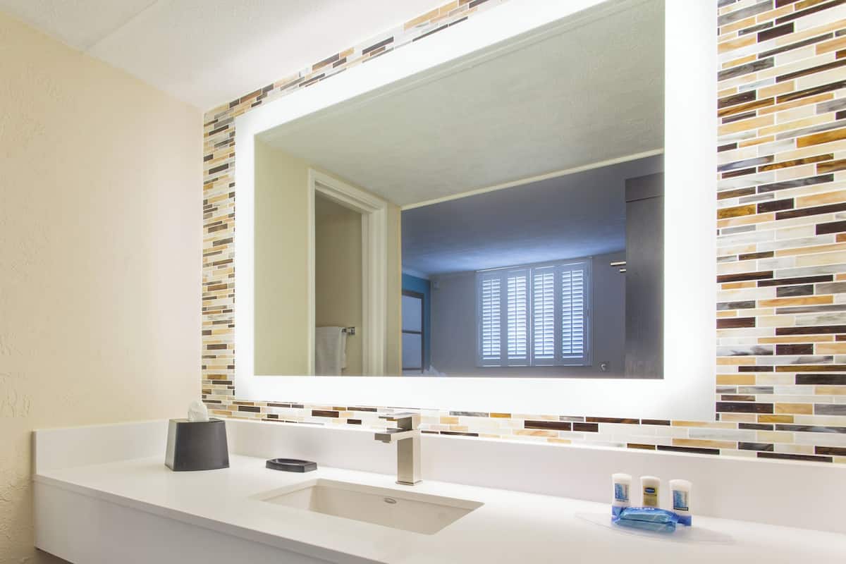 A bathroom with a white sink, a mirror, and a tiled backsplash.