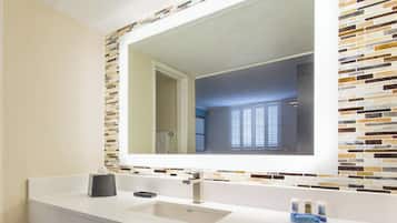 Une salle de bain avec un lavabo blanc, un miroir et un mur recouvert de carreaux.