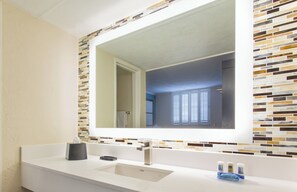 A bathroom with a white sink, a mirror, and a tiled backsplash.