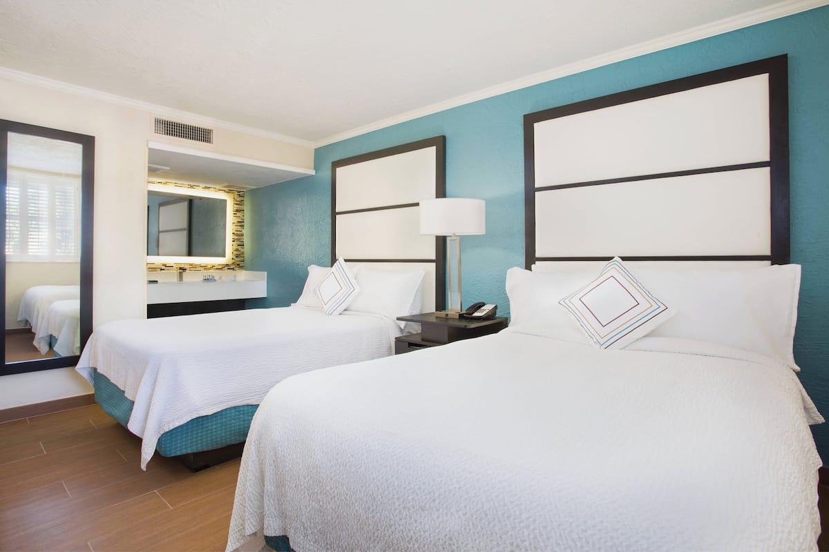 A hotel room with two beds, a bathroom mirror, and a nightstand with a lamp.