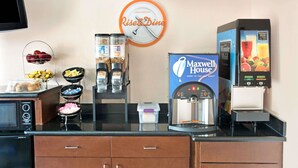 A kitchen area with a clock, coffee machine, and food display. - Howard Johnson by Wyndham Houston Heights/Downtown (Houston)