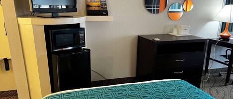 A hotel room with a bed, a TV, a microwave, a small desk, and a mirror wall.