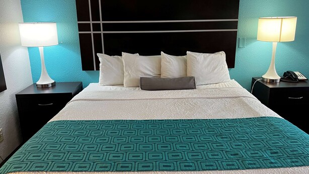 A neatly made bed with white linens and a teal geometric-patterned throw. - Howard Johnson by Wyndham Houston Heights/Downtown (Houston)