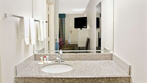 A bathroom with a granite countertop, a sink, a mirror, and a television mounted on the wall. - Howard Johnson by Wyndham Houston Heights/Downtown (Houston)