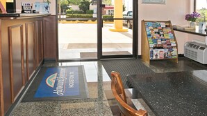 A hotel reception area with a reception desk, a seating area, a bulletin board with brochures, and a view of the outside. - Howard Johnson by Wyndham Houston Heights/Downtown (Houston)