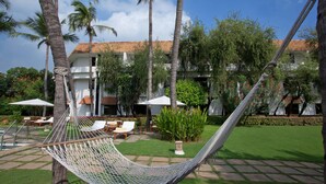Uma rede em um jardim exuberante com palmeiras, um edifício branco com telhado de cerâmica e móveis de exterior.