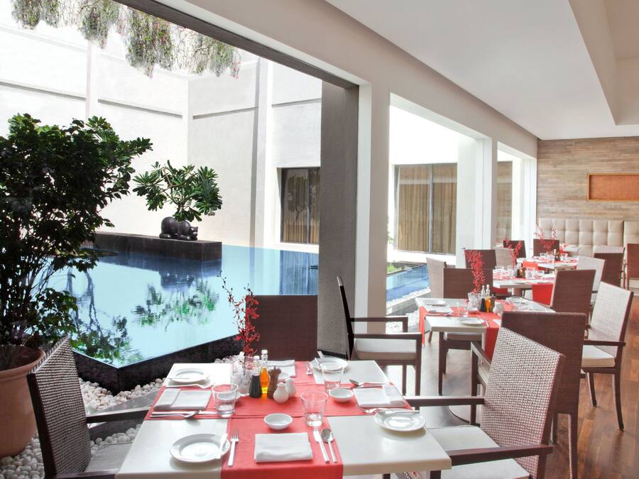 A modern dining area with tables set for two, large windows, and a view of a water feature.