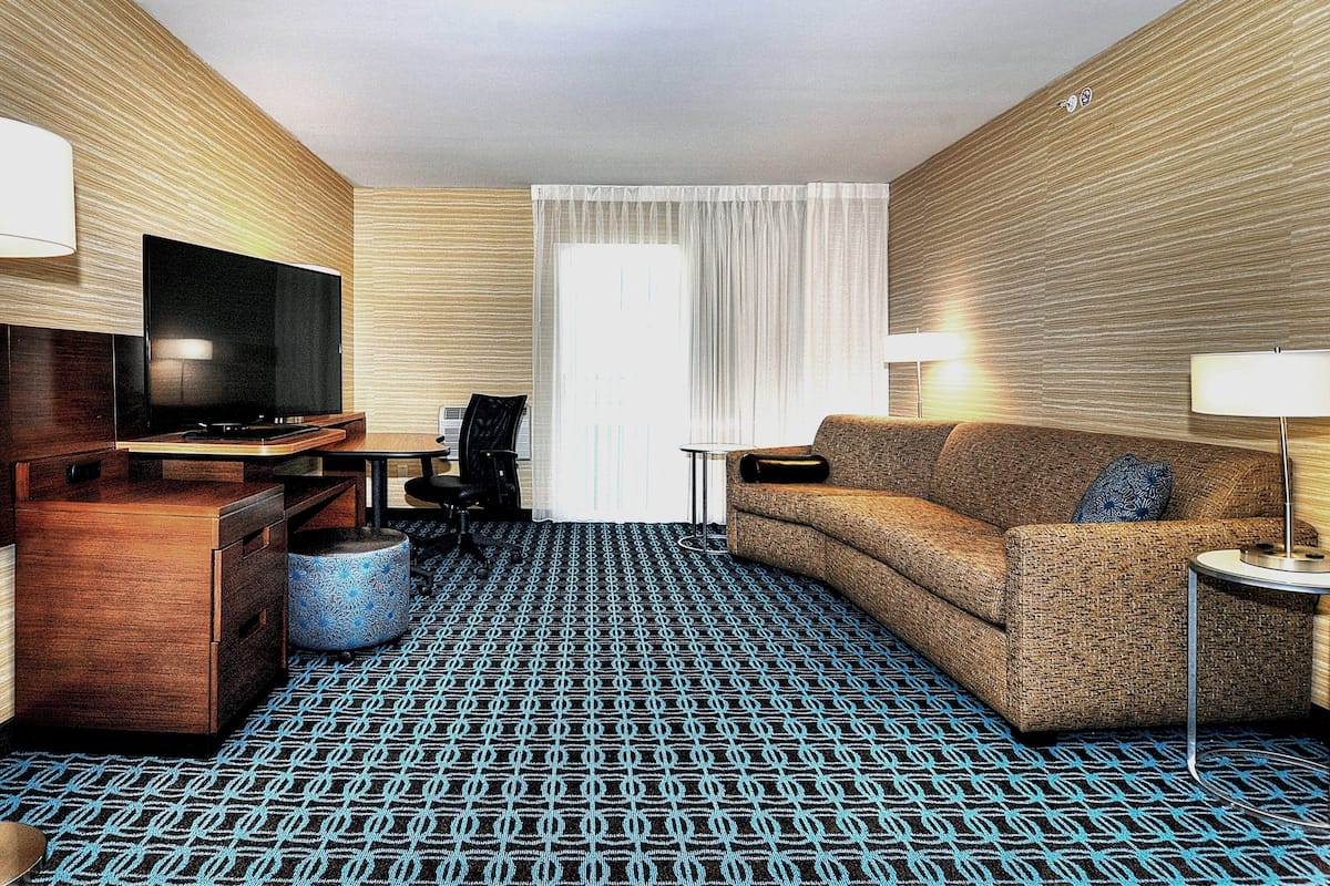 Une chambre d’hôtel équipée d’un téléviseur à écran plat, d’un canapé, d’une petite table, d’une lampe, d’une chaise et d’un tapis à motifs.