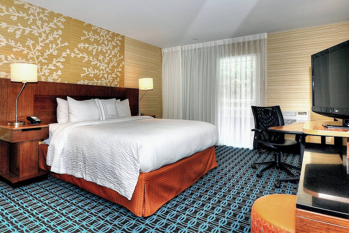 Une chambre d’hôtel avec un grand lit, un bureau avec une chaise, une télévision et une moquette à motifs.