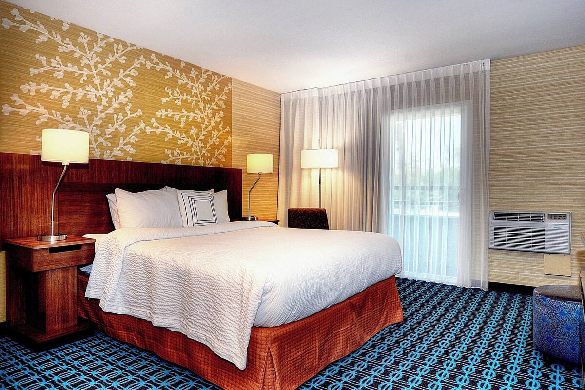 Une chambre d’hôtel avec un grand lit, deux tables de chevet avec des lampes, une fenêtre avec des rideaux et un appareil de climatisation.