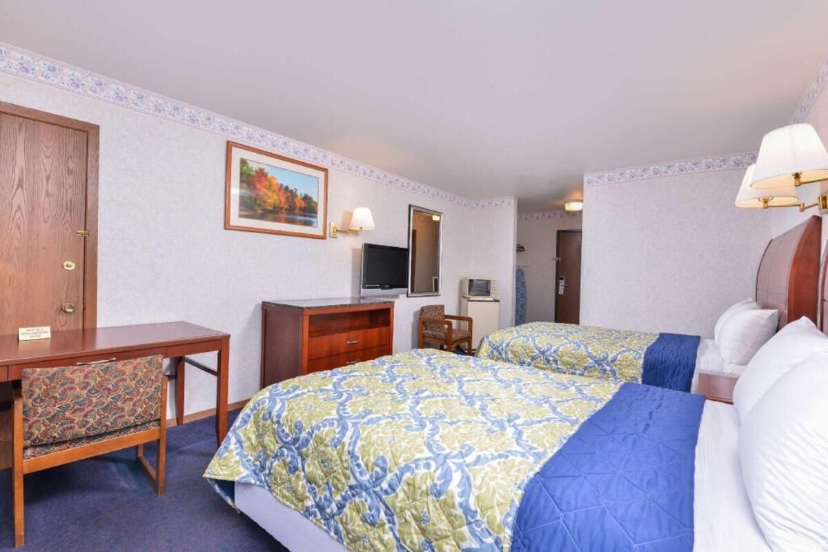 A hotel room with two beds, a desk, a dresser, a TV, and a mirror.