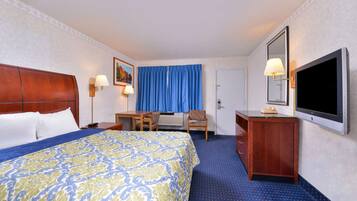 Habitación de hotel con una cama grande, un escritorio, una silla, un aparador, un televisor y una ventana con cortinas azules.