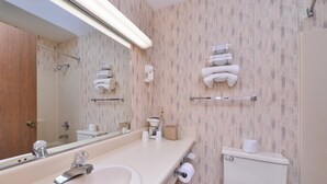 A bathroom with a sink, mirror, towel rack, toilet, and a shower area.