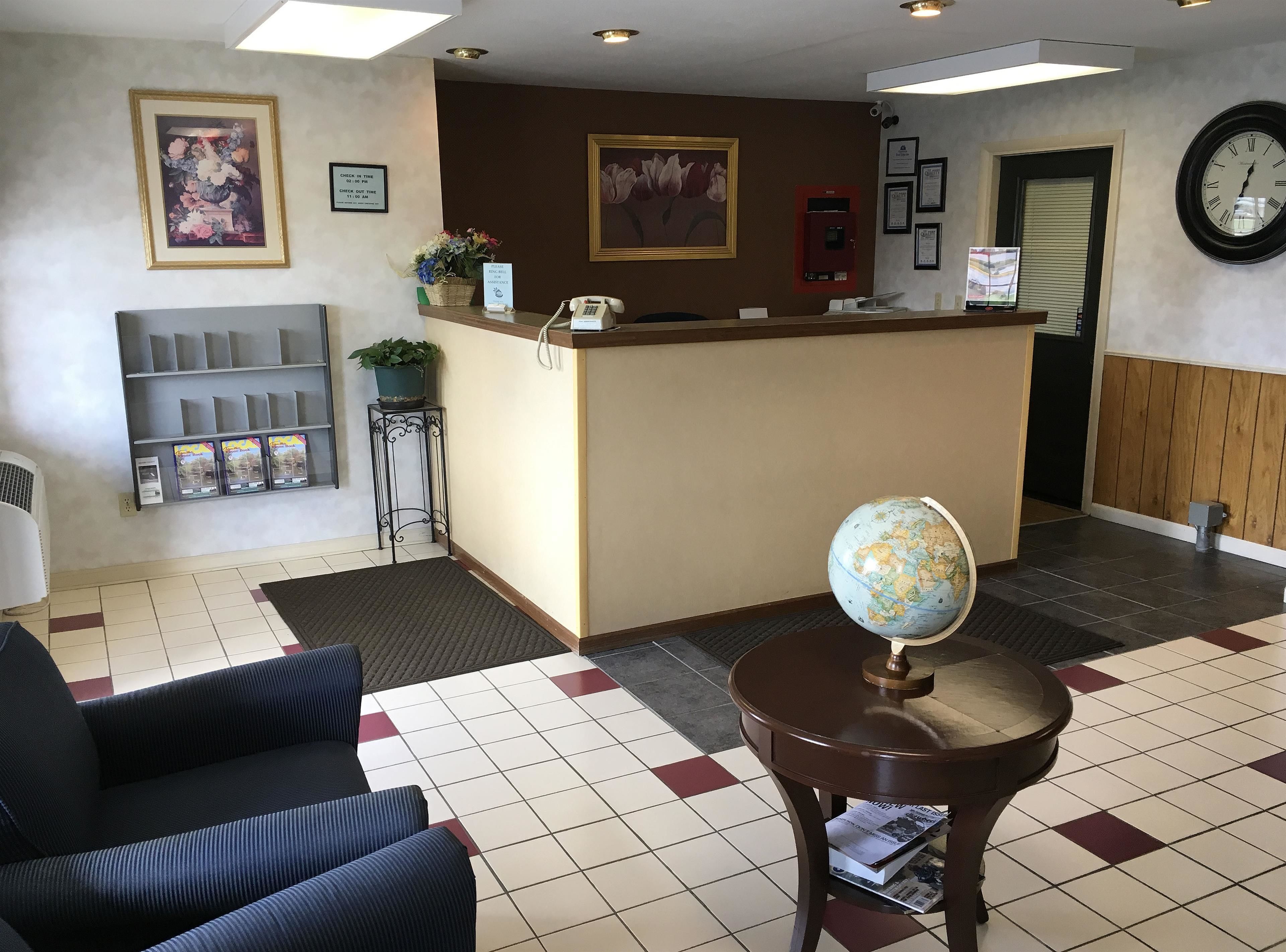 A reception area with a reception desk, a globe, a chair, a small table with a newspaper, and framed artwork on the walls.