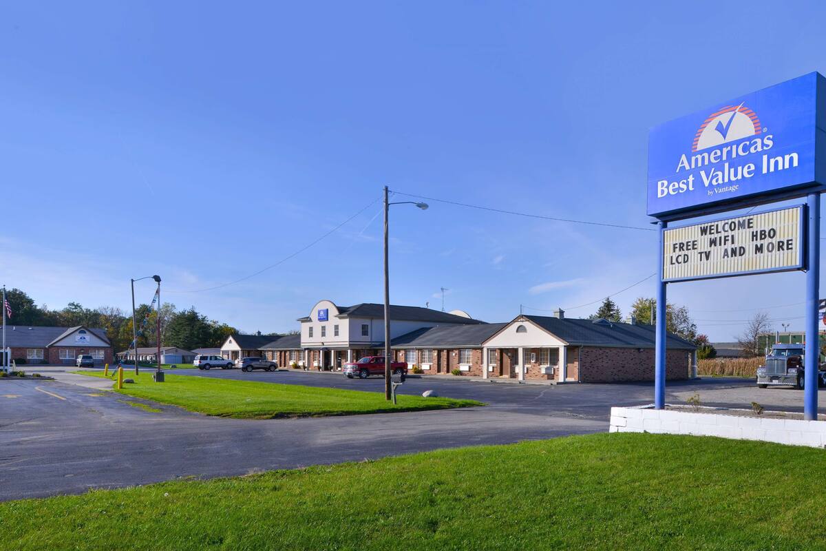 A Best Value Inn with a clear blue sky, parking area, and a signboard advertising free WiFi, TV, and more.