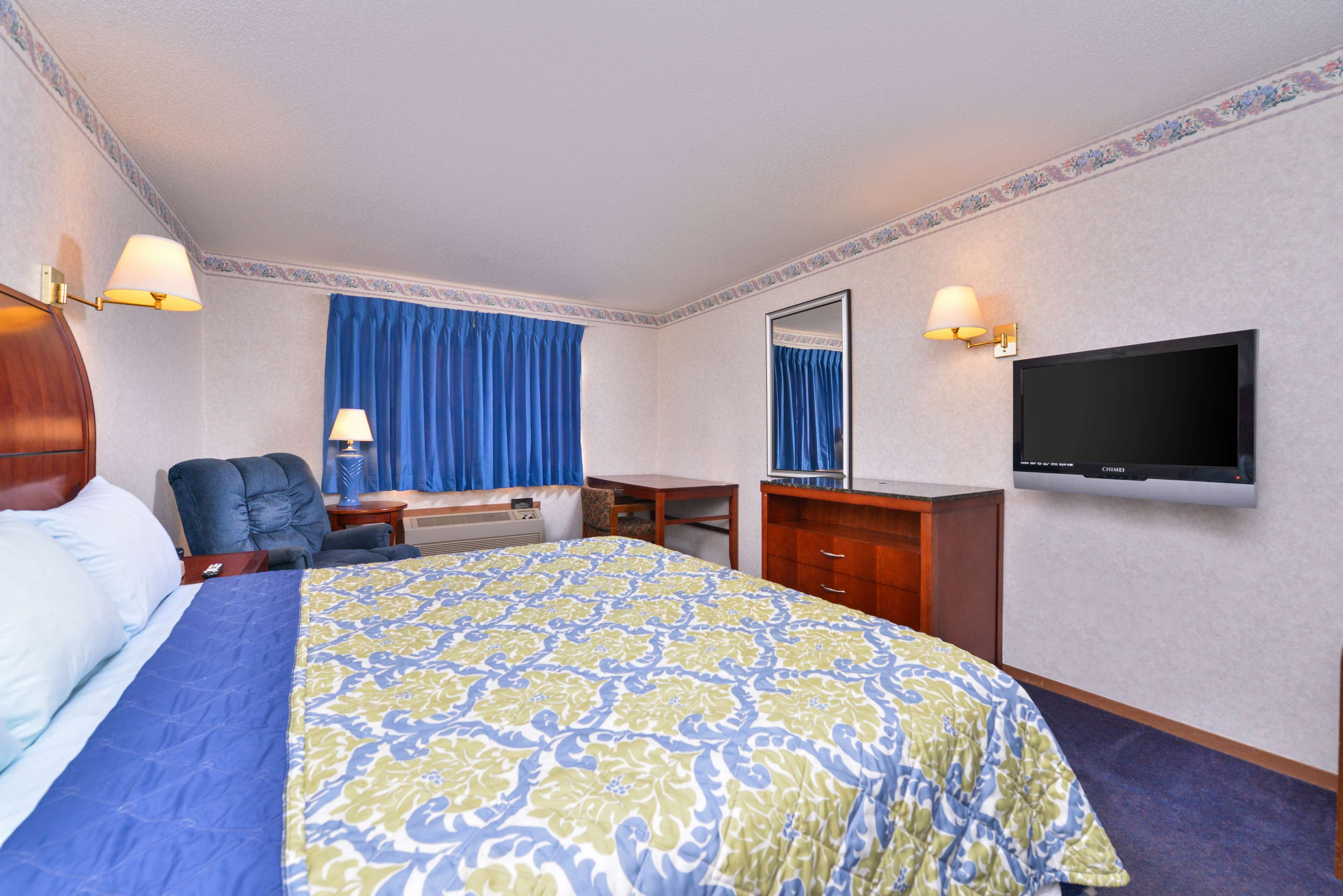 A hotel room with a bed, a desk, a chair, a TV, and a window with curtains.