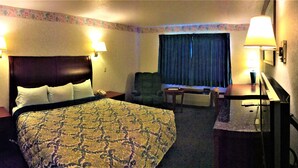 A hotel room with a large bed, two bedside lamps, a chair, a desk with a lamp, and a window with curtains.