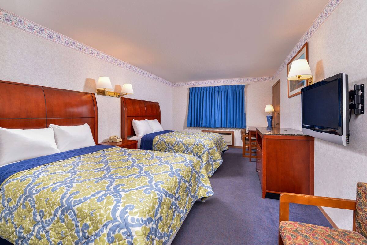 A hotel room with two beds, a desk, a chair, a television, and a window with curtains.