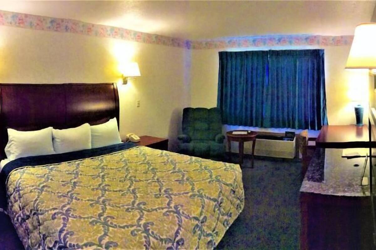A hotel room with a bed, a chair, a desk, a lamp, and a window with curtains.