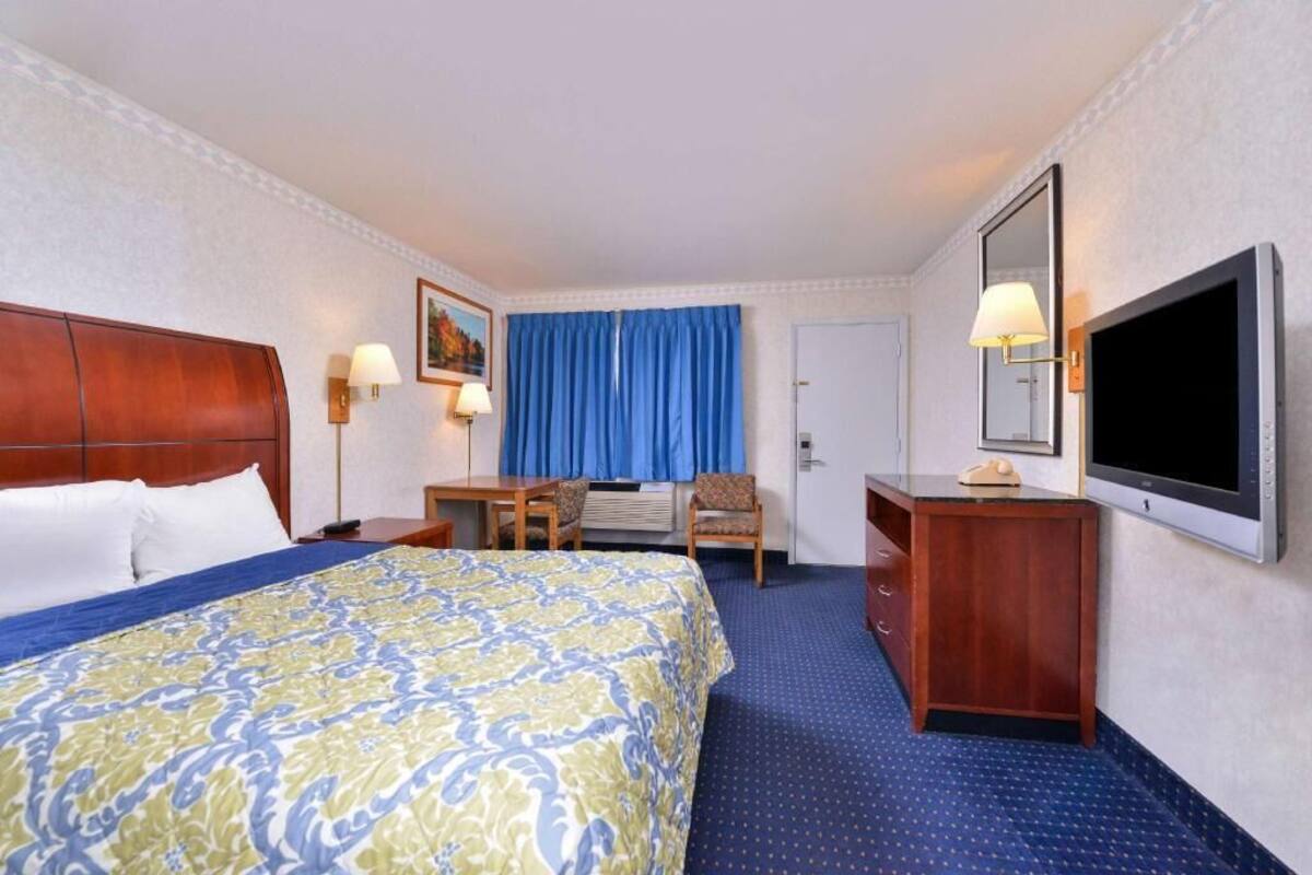 A hotel room with a large bed, a desk, a chair, a dresser, a television, and a door.