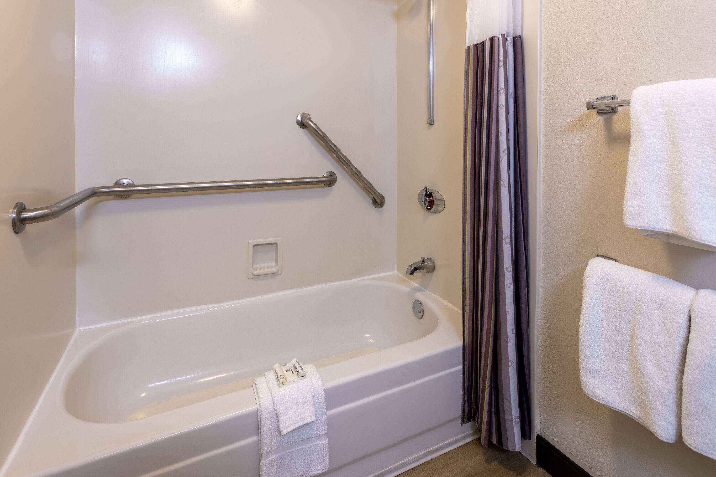 A white bathtub with a grab bar, a towel rack, and a shower curtain.