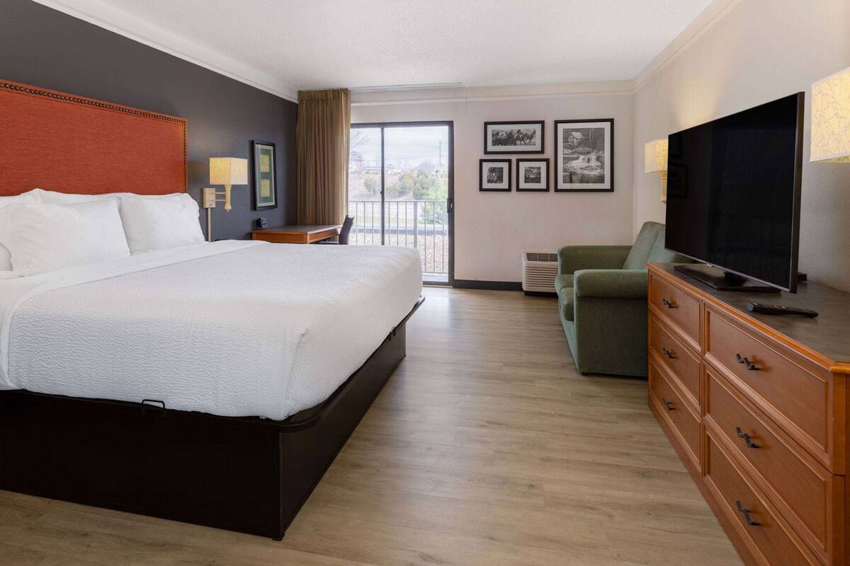 A hotel room with a bed, a television, a dresser, and a window with a view.