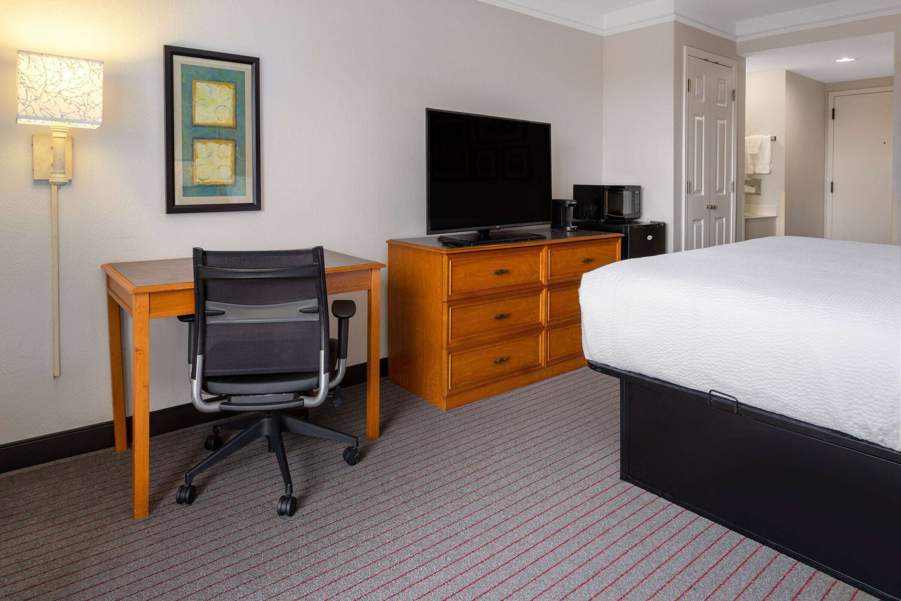 Una habitación de hotel con una cama, un escritorio con silla, un televisor y un aparador.