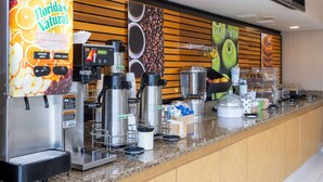 Un espace café en libre-service comprenant plusieurs machines à café, un distributeur de jus et une variété d’aliments disposés sur un comptoir.