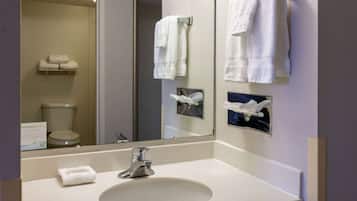 Un baño con lavamanos, espejo y toallas en toalleros.