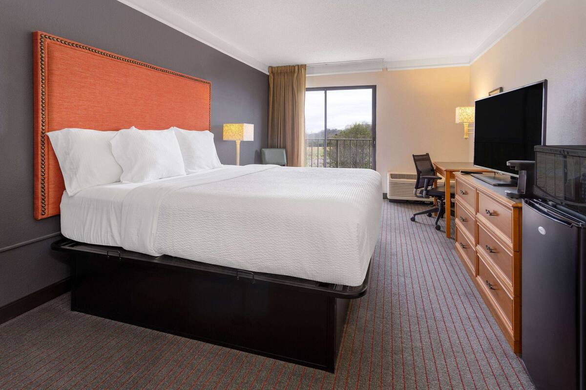 A hotel room with a large bed, a desk with a television, and a view of the outdoors.