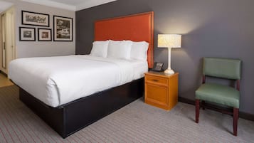 A hotel room with a bed, a nightstand with a lamp, a chair, and framed pictures on the wall.