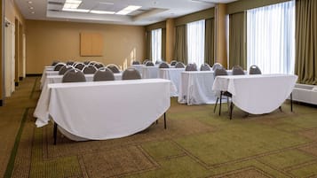 A conference room with tables and chairs, carpeted floor, and large windows with curtains.