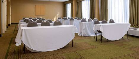 A conference room with tables and chairs, carpeted floor, and large windows with curtains.