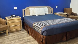 A hotel room with a large bed, a nightstand with a phone, a chair, and a wooden floor. - Lake Place Inn (Lake Havasu City)