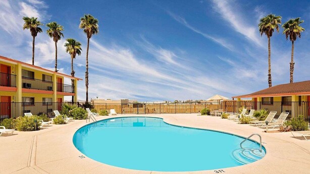 A swimming pool with lounge chairs and palm trees, surrounded by a building with balconies. - Lake Place Inn (Lake Havasu City)