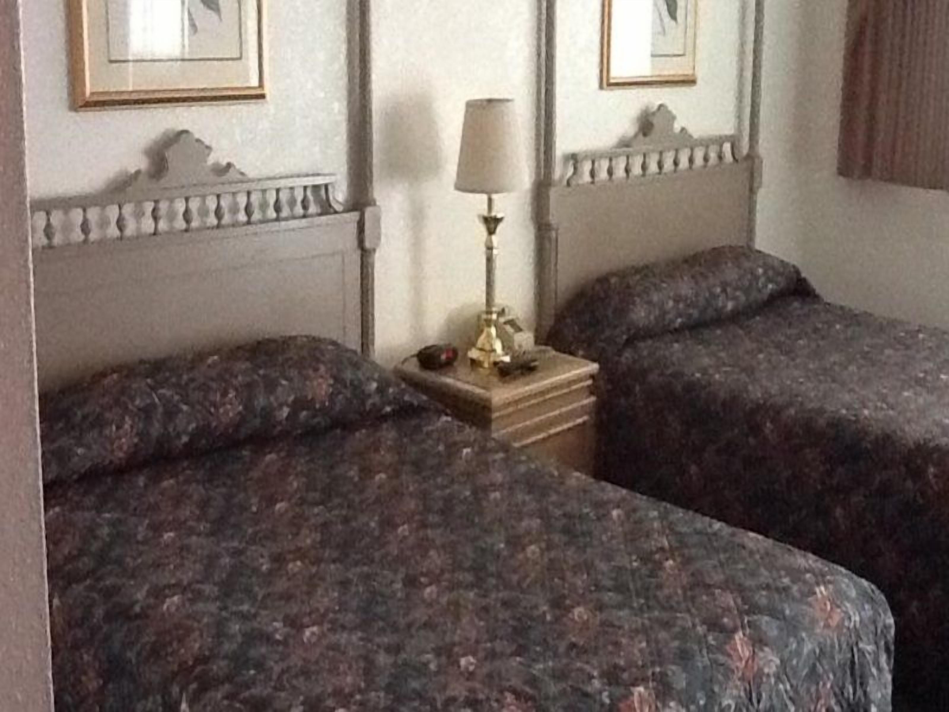 A room with two beds, a nightstand with a lamp, and framed pictures on the wall.