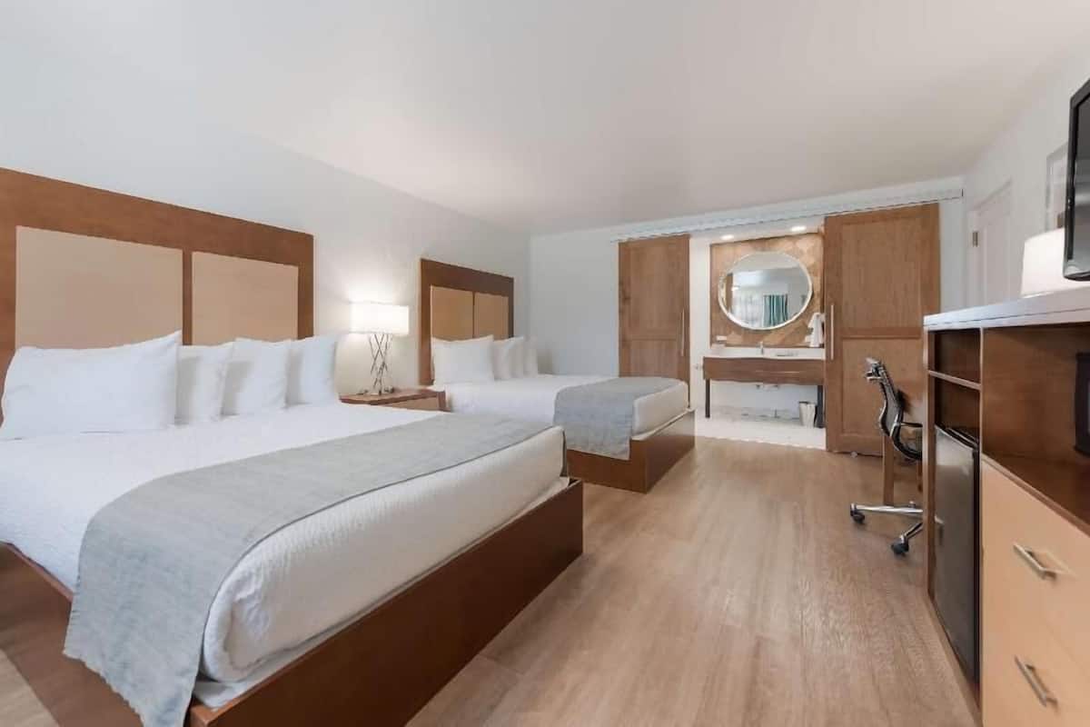 A hotel room with two beds, a desk, a mirror, and a wardrobe.