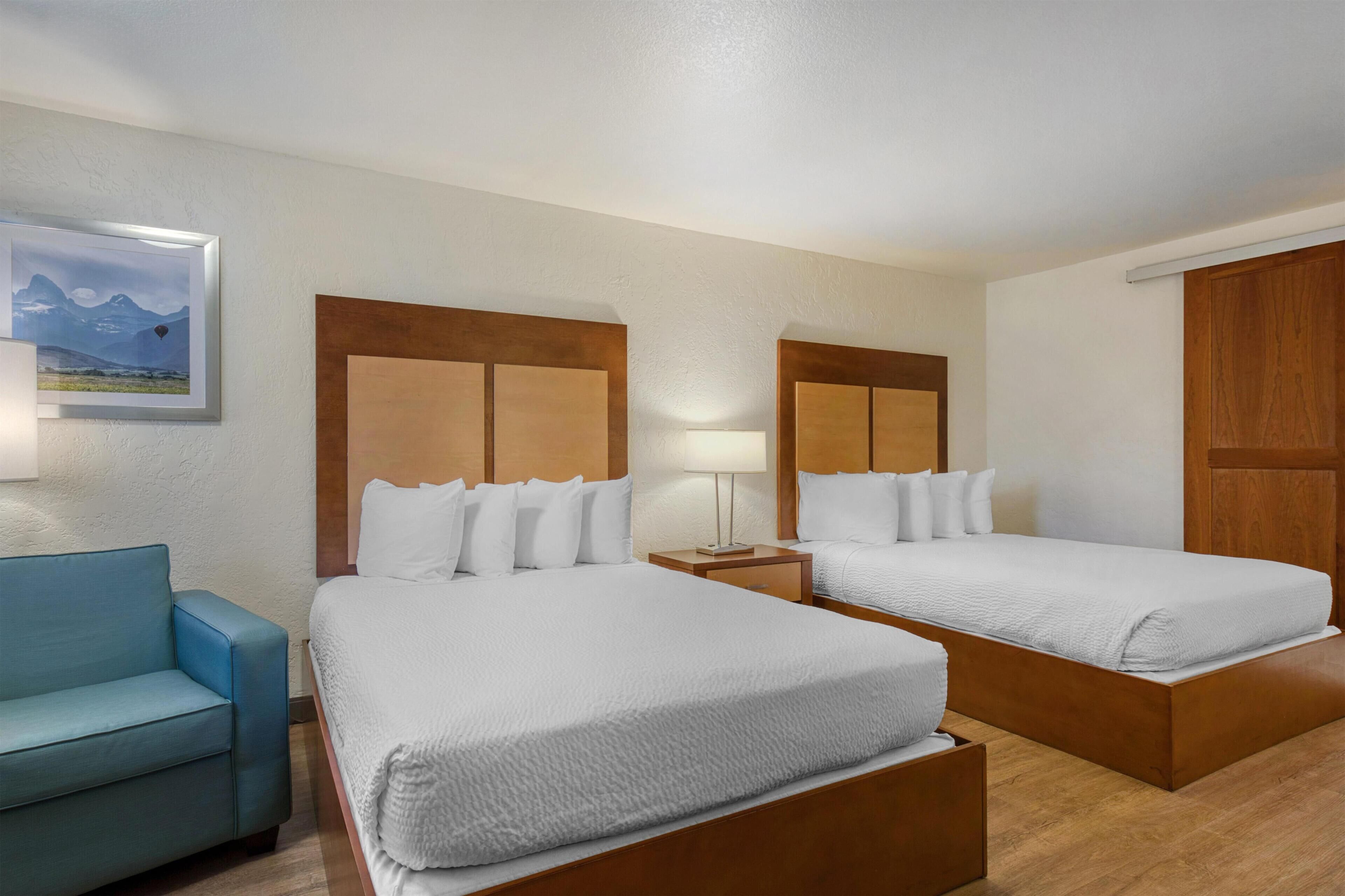 A hotel room with two beds, a blue sofa, a nightstand with a lamp, and a framed picture on the wall.