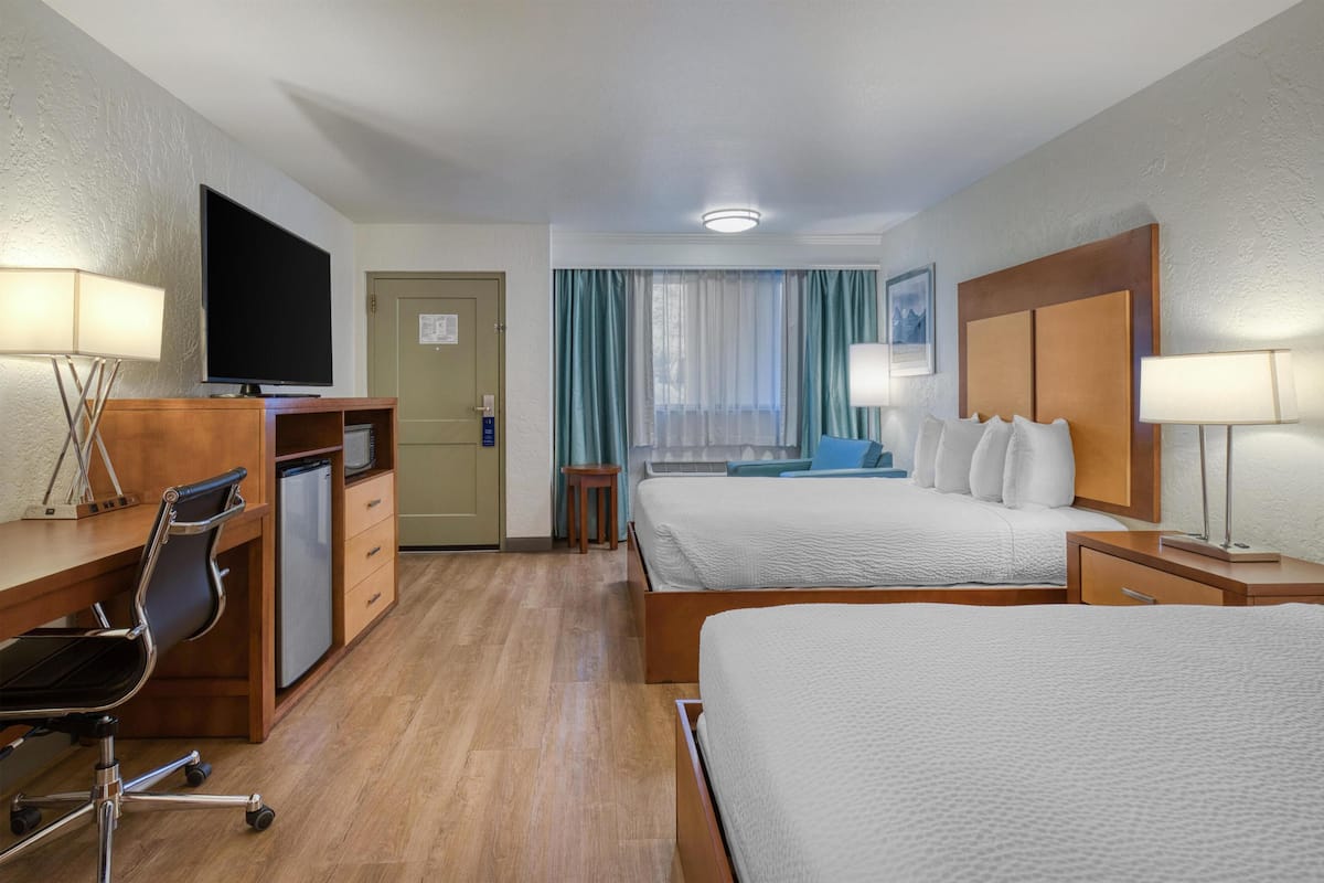A hotel room with a bed, desk, chair, TV, and a window with curtains.