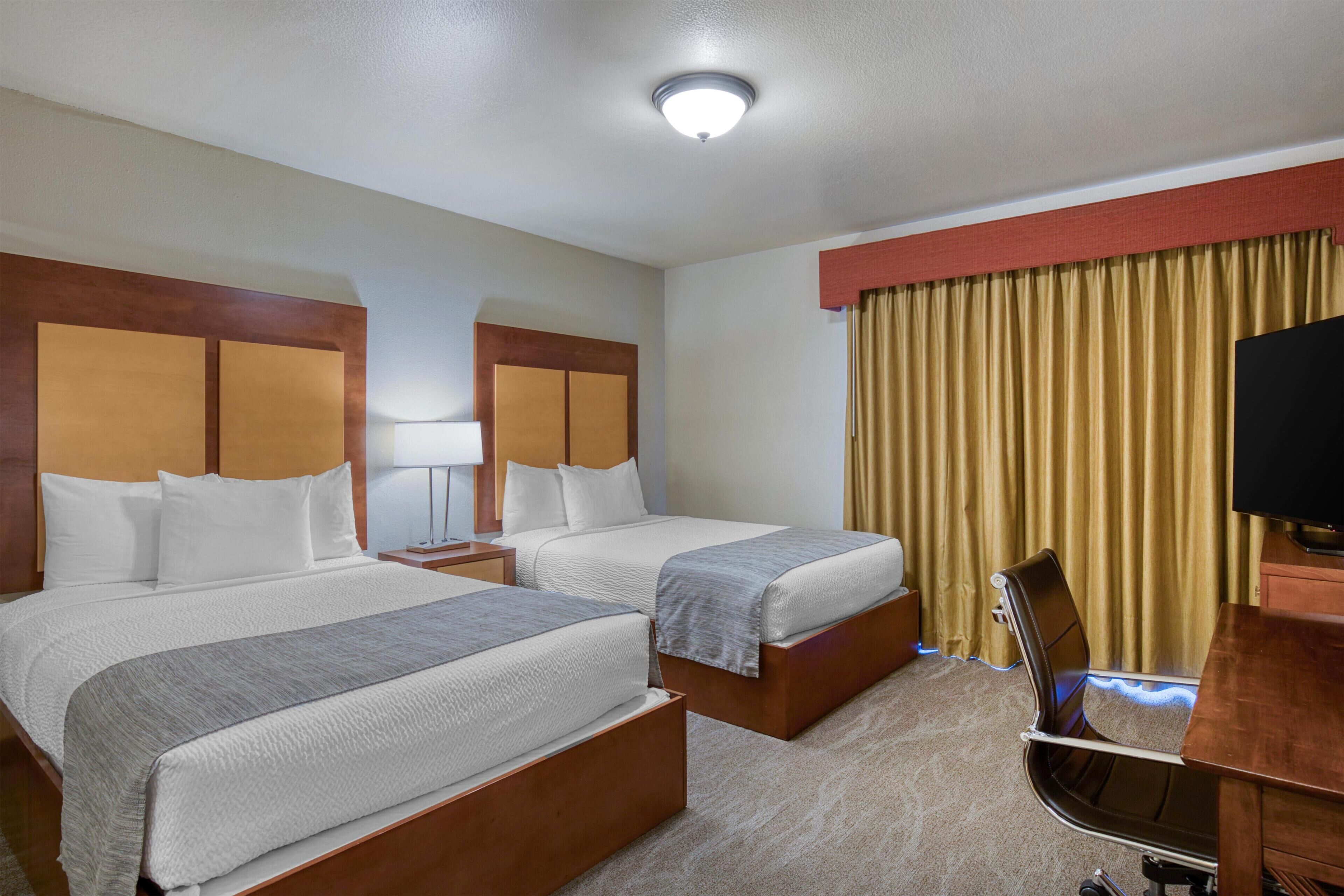 Habitación de hotel con dos camas, un escritorio, una silla, un televisor y una ventana con cortinas.