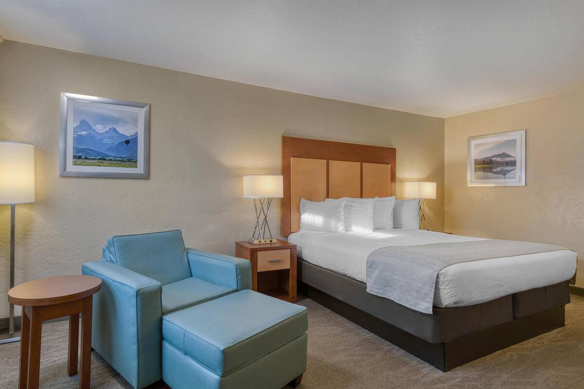 A hotel room with a bed, two chairs, a small table, two bedside lamps, and two framed pictures on the walls.