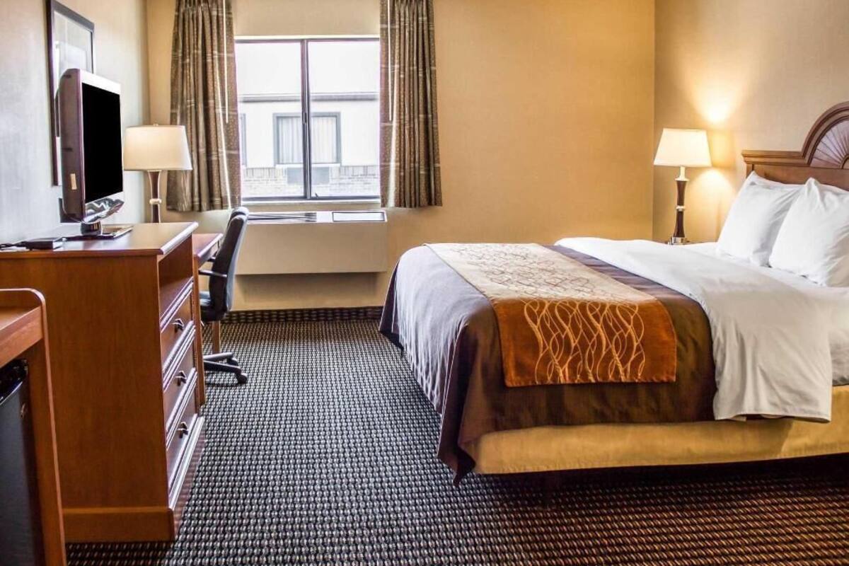 A hotel room with a bed, desk, chair, TV, and window with curtains.