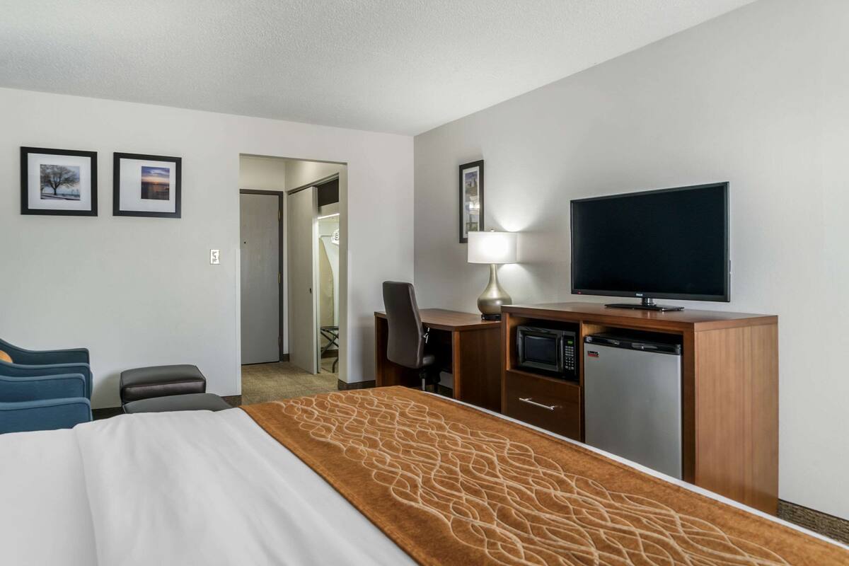 A hotel room with a bed, a desk with a computer, a television, and a microwave.