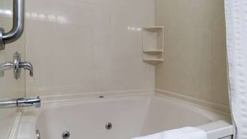 A bathroom with a bathtub, a handrail, and a small shelf.