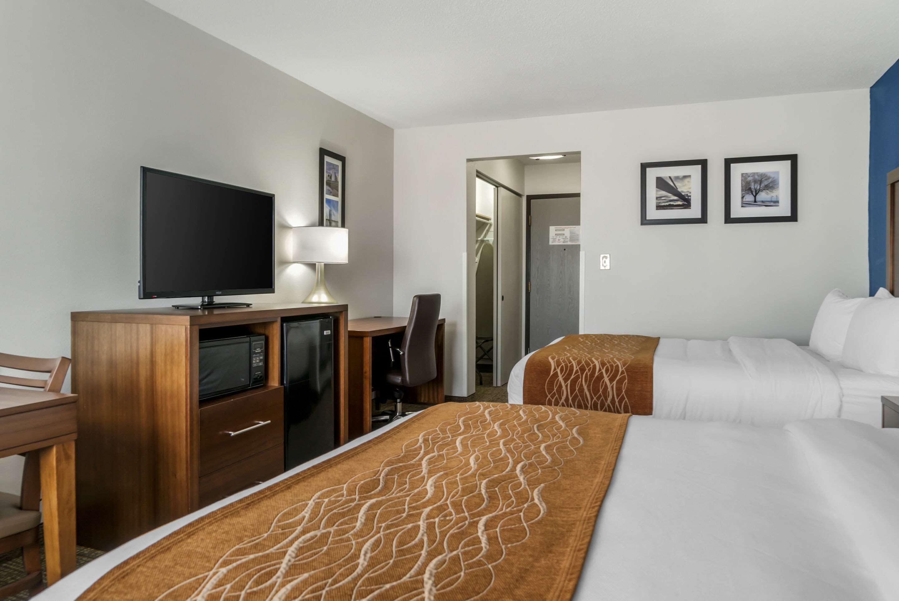 A hotel room with a TV, desk, two beds, and a door leading to a bathroom.