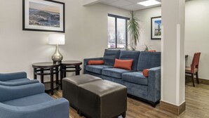 A modern living room with a blue sofa, a brown ottoman, and a round table with a lamp.
