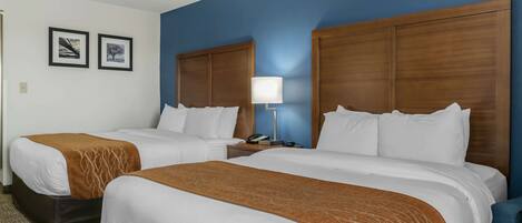 A hotel room with two beds, a nightstand with a lamp, and two framed pictures on the wall.