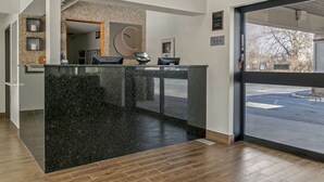 A reception desk with a black marble counter, a wooden floor, and a view of the street through a glass door.