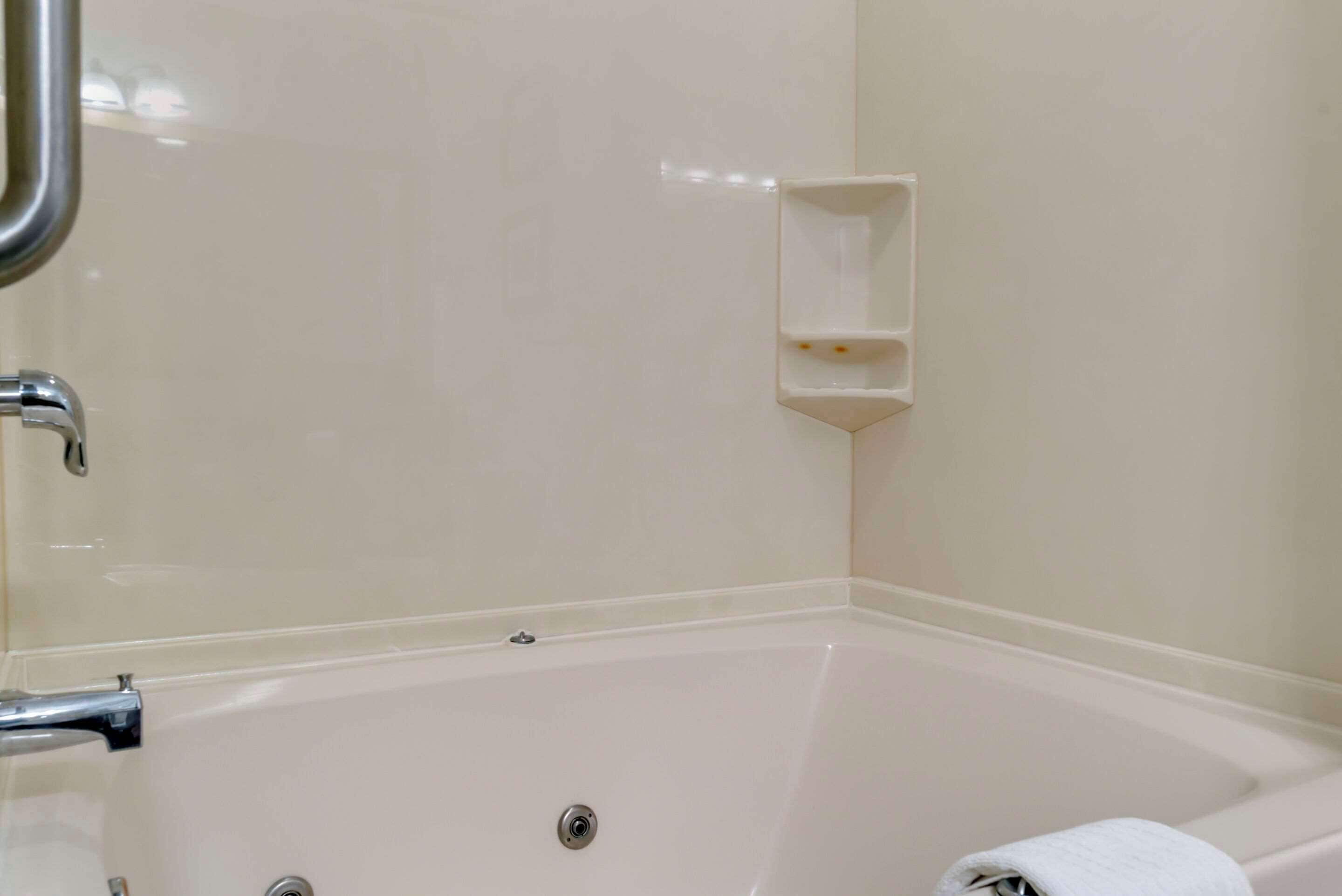 Un baño con una bañera blanca, un grifo cromado y un pequeño estante sobre la bañera.